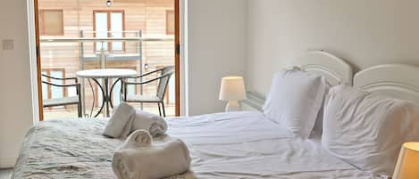A bedroom with a bed, pillows, a bedside lamp, and a view of an outdoor area with a table and chairs.