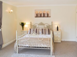 A neatly arranged bedroom with a metal-framed bed, two bedside tables, a nightstand, and a wall-mounted lamp.