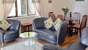 A living room with two blue leather sofas, a glass coffee table, and a dining table with chairs. - Rosecraddoc Manor - Riverview (Near Liskeard)