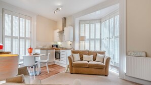 A modern living room with a beige sofa, a dining table with chairs, and a kitchen area with white cabinets and a stove. - 2 bedroom accommodation in Whitby (Whitby)