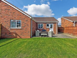 A brick house with a patio, a barbecue area, and a fenced yard. - Lovely modern bungalow only minutes from the sand dunes at Beadnell Bay. (Beadnell)