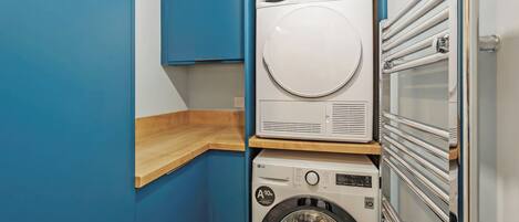 A compact laundry room with a stacked washer and dryer, wooden counter, and blue walls.