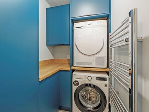 A compact laundry room with a stacked washer and dryer, wooden counter, and blue walls.