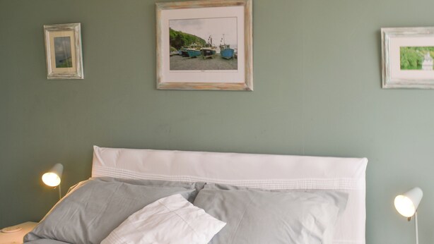 A neatly made bed with white bedding and pillows, a framed picture of boats on the wall, and bedside lamps on either side.