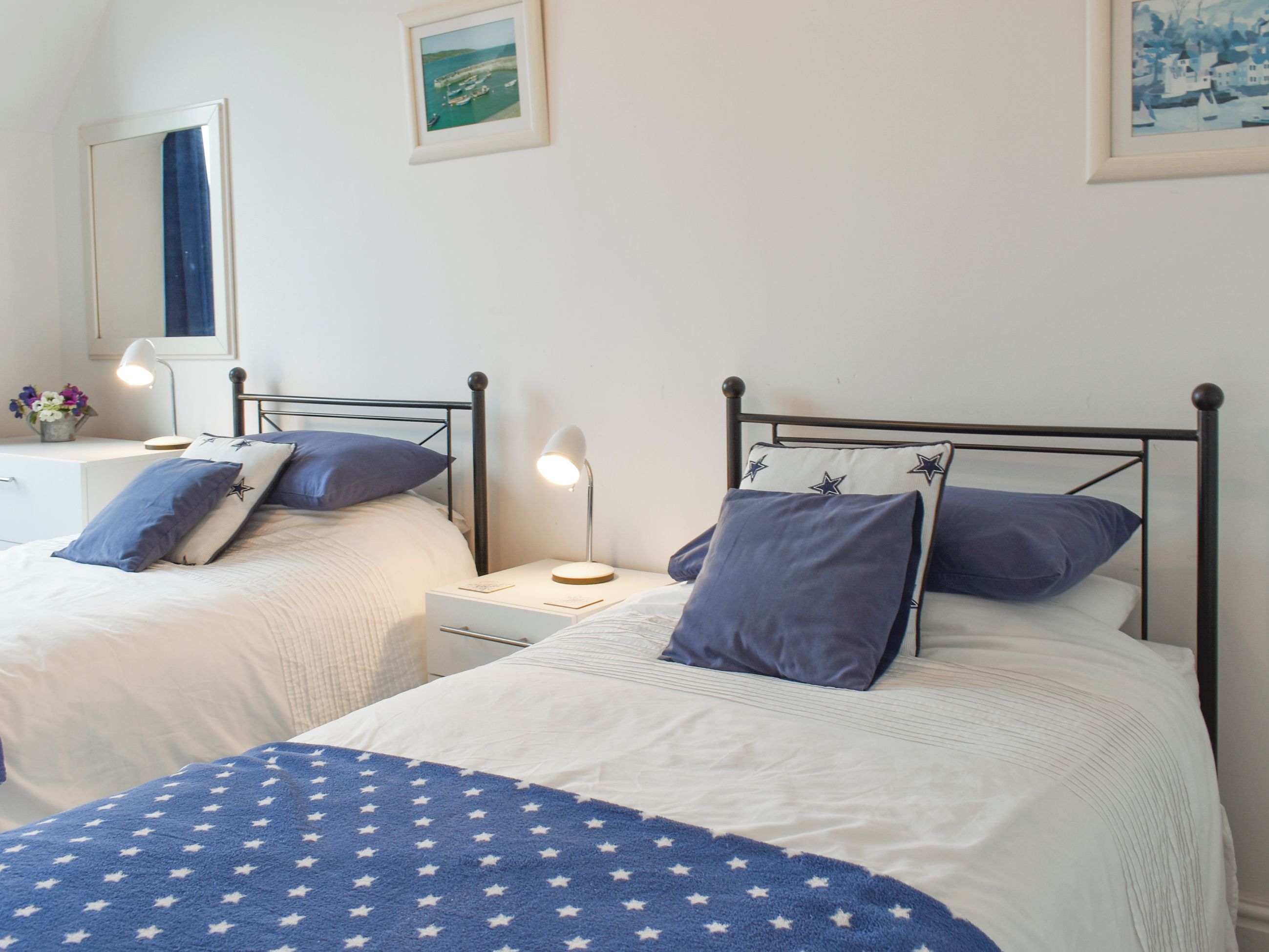 A bedroom with two single beds, each with a nightstand, a lamp, and a framed picture on the wall.