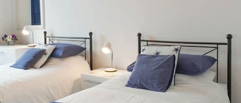 A bedroom with two single beds, each with a nightstand, a lamp, and a framed picture on the wall.