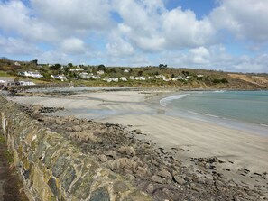 Une plage côtière avec un premier plan rocheux, une rive sablonneuse et des maisons en arrière-plan.