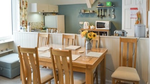 A dining area with a wooden table and chairs, a vase with sunflowers, and a kitchen in the background.