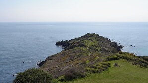 A coastal landscape with a grassy hill and a clear view of the sea.