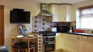 A compact kitchen with a gas stove, microwave, and a small dining area with a table and two stools. - Explore North Yorkshire from this cosy, dog-friendly former stable near Thirsk. (South Kilvington near Thirsk)