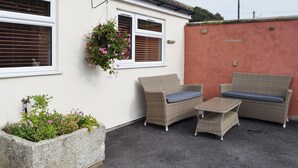 A patio area with wicker furniture, a hanging flower pot, and a stone planter with flowers. - Explore North Yorkshire from this cosy, dog-friendly former stable near Thirsk. (South Kilvington near Thirsk)