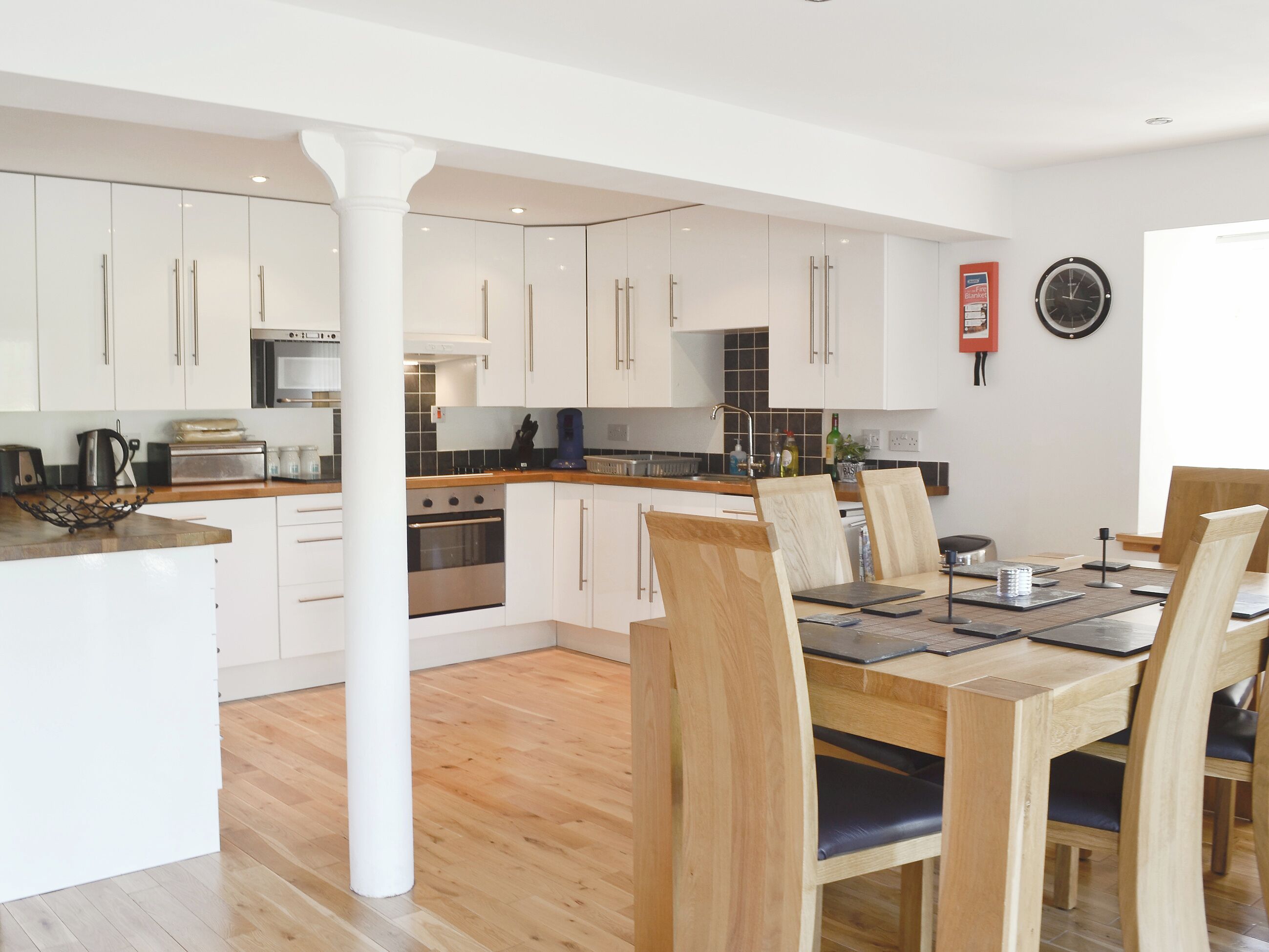 A modern kitchen with white cabinets, a central island, and a dining area with wooden chairs and a table.