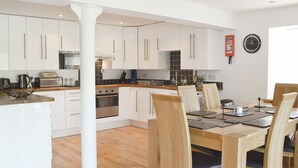 Une cuisine moderne avec des meubles blancs, un îlot central et un coin repas comprenant des chaises et une table en bois.