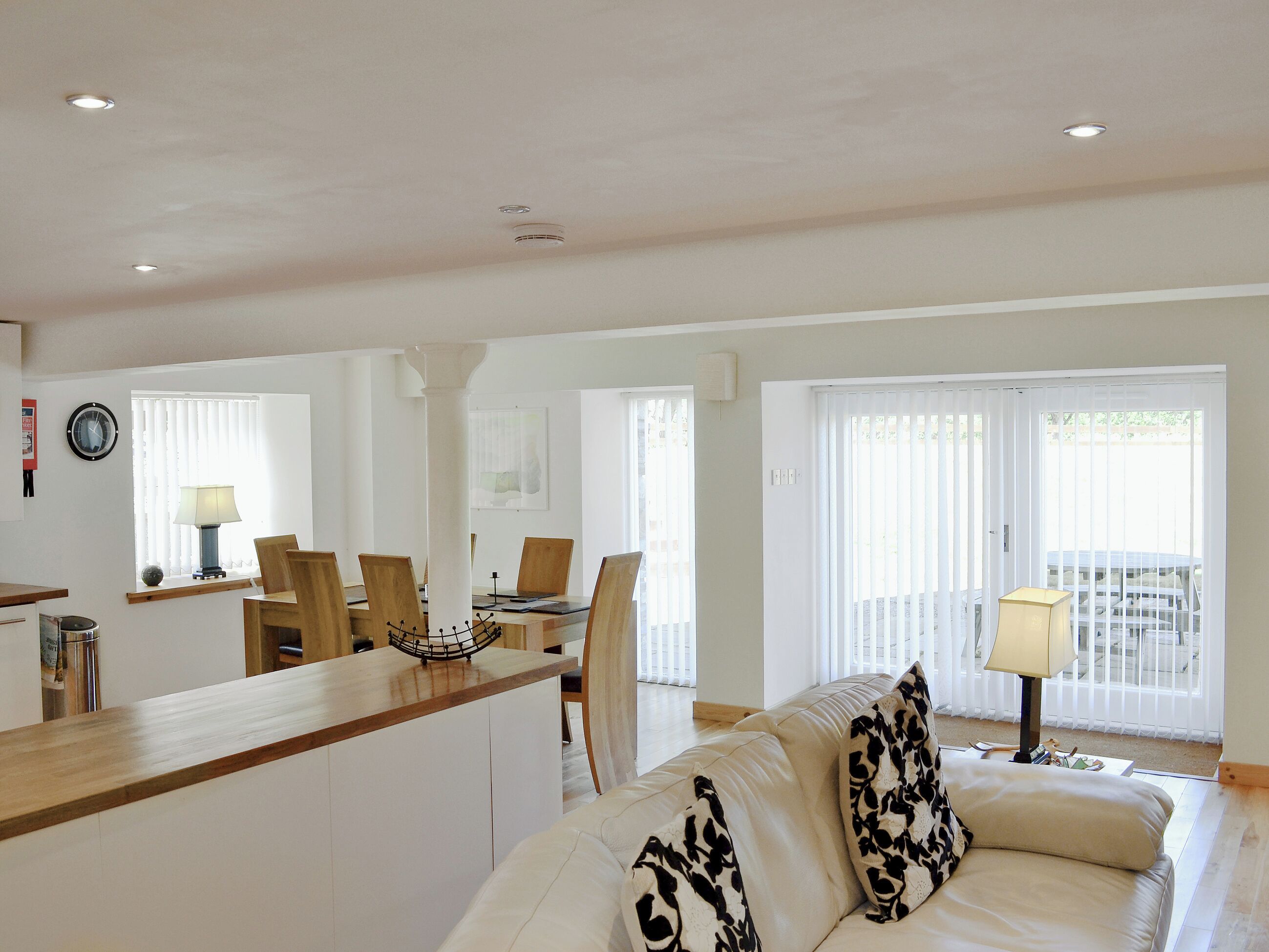 A spacious living area with a sofa, a dining table with chairs, a kitchen counter, and a view through large windows.