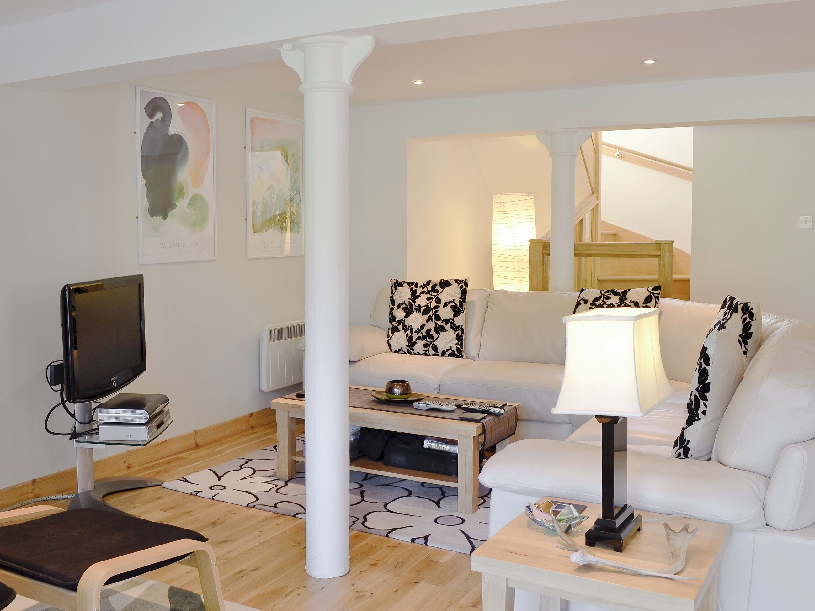 A modern living room with a flat-screen TV, a white sofa, a coffee table, and a lamp.