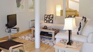 Un salon moderne avec un téléviseur à écran plat, un canapé blanc, une table basse et une lampe.