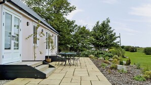 A building with a paved patio, outdoor seating, and a garden area with trees and shrubs. - 2 bedroom accommodation in Clachan near Tarbert (Clachan near Tarbert)