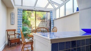 A conservatory with a tiled floor, wooden chairs, a table, and a view of a garden through a glass door. - 4 bedroom accommodation in Cleobury Mortimer, near Ludlow (Cleobury Mortimer, near Ludlow)