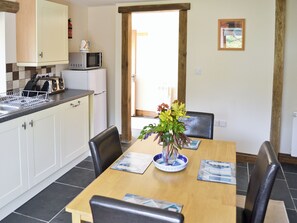 A dining area with a wooden table, chairs, a vase of flowers, and a kitchen in the background. - 1 bedroom accommodation in Hartland, near Bideford (Hartland, near Bideford)