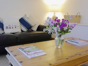 Uma sala de estar com sofá, mesa de centro com revistas e um vaso com flores.