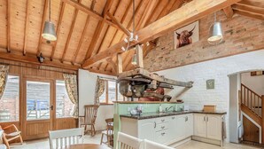 Cocina rústica con vigas de madera, zona de comedor con sillas blancas y pared de ladrillo.