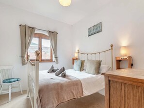 A bedroom with a bed, a chair, a window with curtains, a bedside table, and a lamp.