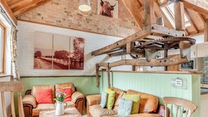 Un interior rústico con vigas de madera a la vista, pared de ladrillo, sofá tapizado en verde, mesa de madera y un cuadro grande de un toro.