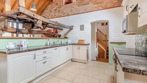 Una cocina con armarios blancos, techo de madera y pared de ladrillo.