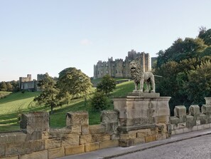 A stone lion statue on a pedestal, a castle in the background, and a grassy hill.