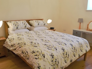 Un lit bien fait, avec une literie à motifs floraux, des lampes de chevet, une radio et une petite table de chevet.