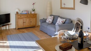 Ein Wohnzimmer mit Fernseher, Holzschrank, Sofa und einem Esstisch mit Flasche und Gläsern.