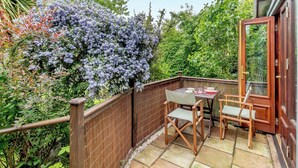 A small patio with a table and chairs, surrounded by a wooden fence and lush greenery. - 2 bedroom accommodation in Woodbridge (Woodbridge)