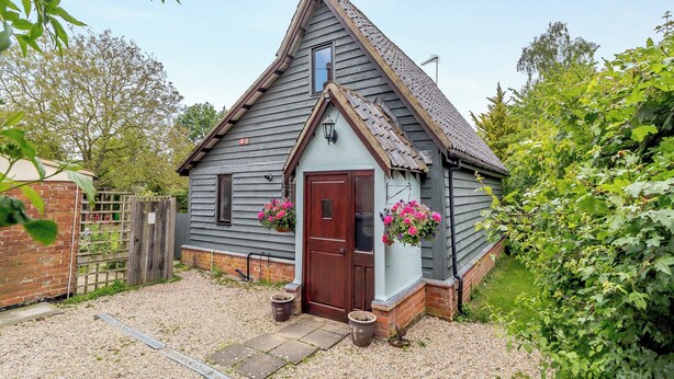 A small, single-story house with a steeply pitched roof, a wooden door, and a small porch area with potted plants. - 2 bedroom accommodation in Woodbridge (Woodbridge)