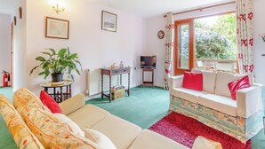 A living room with a sofa, a television on a stand, a potted plant, and a window with curtains. - 2 bedroom accommodation in Woodbridge (Woodbridge)
