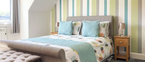 A bedroom with a bed, a nightstand, a lamp, a window with curtains, and a radiator.