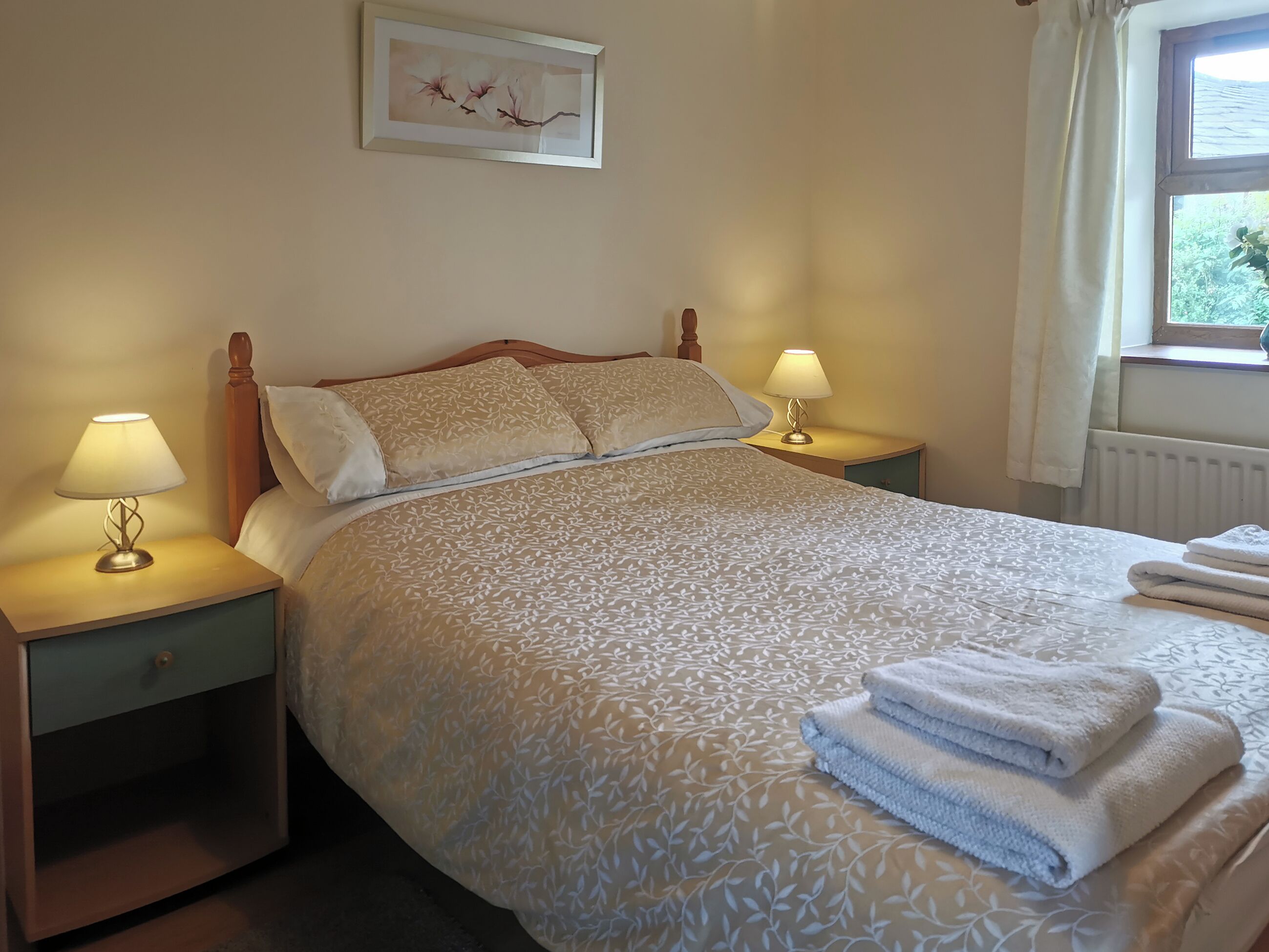 A neatly made bed with a patterned bedspread, two bedside lamps, and a framed artwork on the wall.