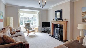 Een woonkamer met een bank, een open haard, een televisie en een groot raam.