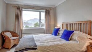 Een slaapkamer met een groot bed, een houten hoofdbord, een rieten stoel en een raam met gordijnen.