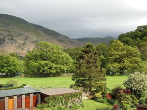 Un paysage rural avec une maison entourée d’une végétation luxuriante et des collines en arrière-plan.