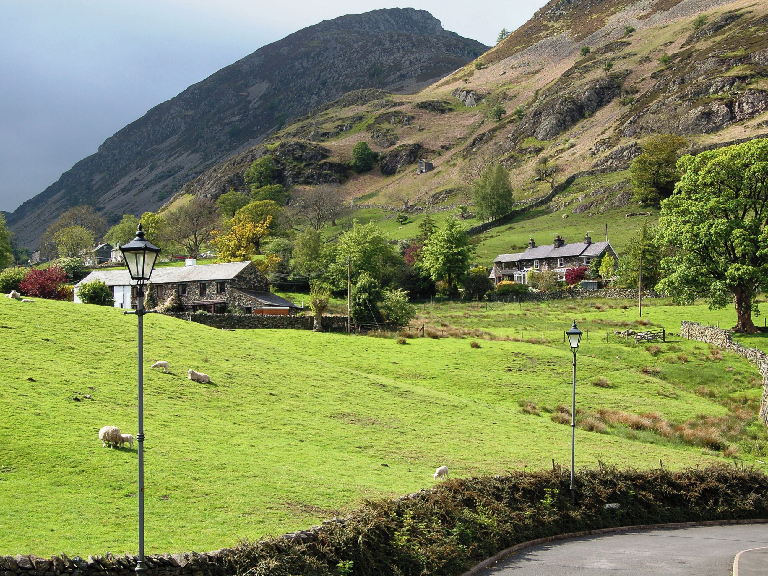 Ländliche Landschaft mit Steinhäusern, einer Steinmauer und einer Wiese mit Schafen.