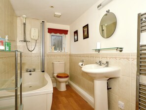 Un baño con bañera, inodoro, lavamanos y una ventana con un cortinero rojo.