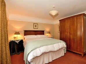 Un dormitorio ordenado con un armario de madera, dos lámparas de noche, una cama con ropa blanca y una pared con diseño.