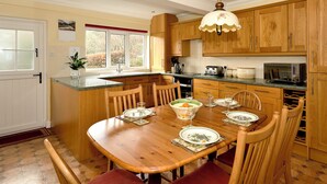 Una cocina con armarios de madera, una mesa de comedor preparada para cuatro comensales y una ventana con vista a árboles.