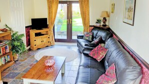 A living room with a leather sofa, a wooden coffee table, a television on a wooden stand, a bookshelf, and a door leading outside. - 2 bedroom accommodation in Hemingby, near Horncastle (Hemingby, near Horncastle)