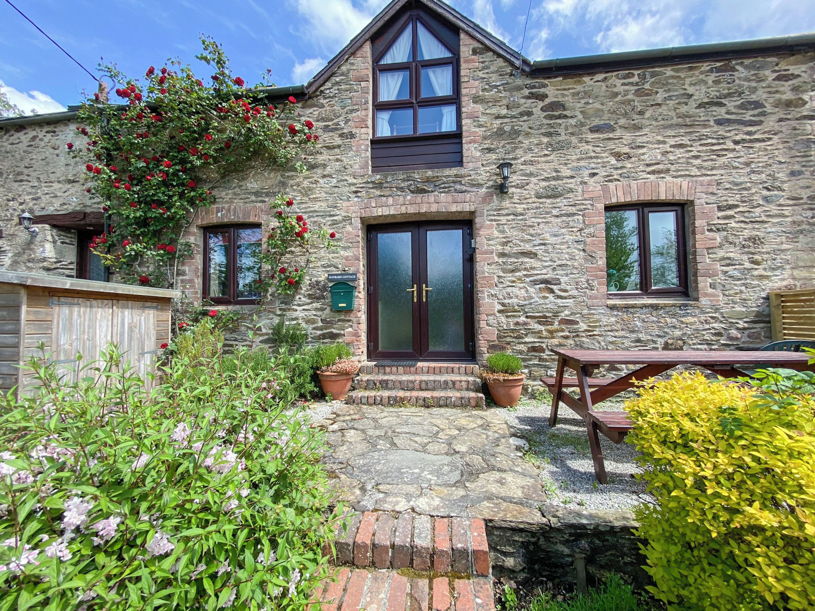 A stone cottage with a wooden door, a small porch, and a bench.