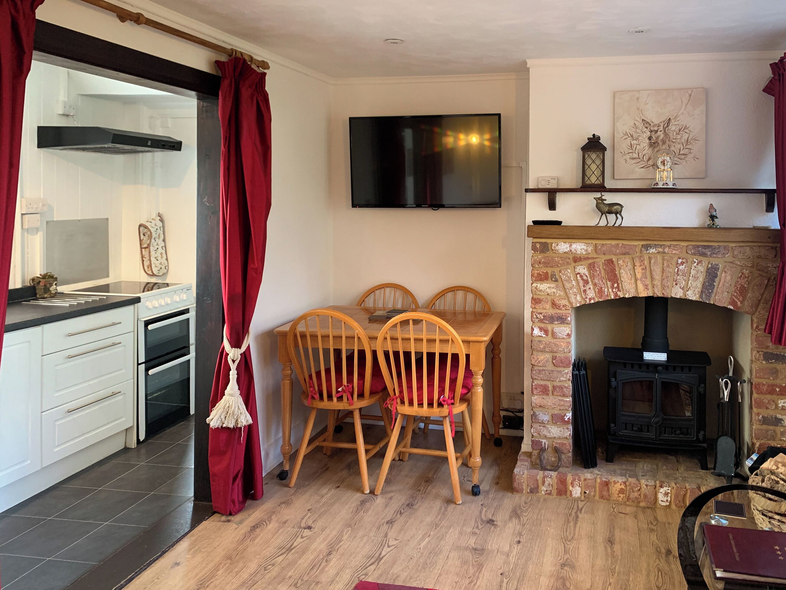 A cozy living room with a fireplace, a dining table with chairs, a TV mounted on the wall, and a kitchen area with cabinets and a stove.