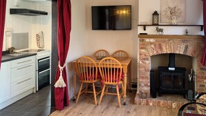 Un salon chaleureux avec une cheminée, une table à manger avec des chaises, un téléviseur fixé au mur et un coin cuisine avec des placards et une cuisinière.