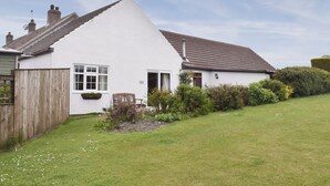 Une maison blanche avec un toit en pente, une clôture en bois et une pelouse bien entretenue.