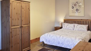 A bedroom with a bed, wooden wardrobe, nightstand, and a framed floral artwork on the wall.