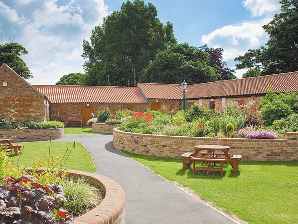 A courtyard with brick buildings, a paved walkway, and outdoor seating areas. - Padgett Lodge - 23052 (Filey)